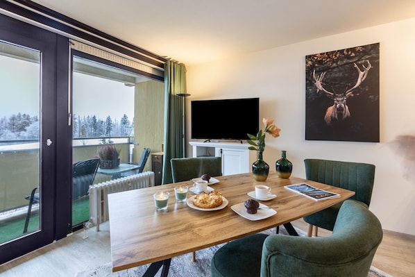 A dining area with a wooden table, chairs, a TV, and a painting on the wall.