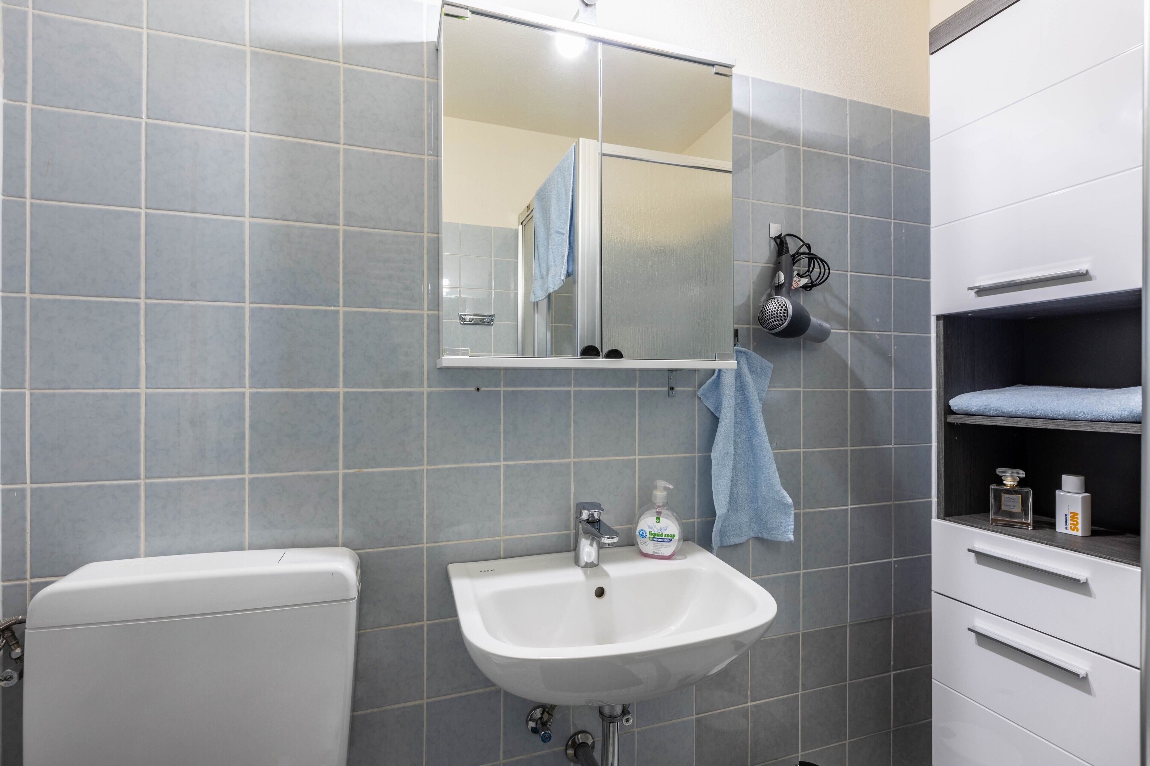 A bathroom with a white sink, a mirror, a towel hanging on the wall, and a shower area.