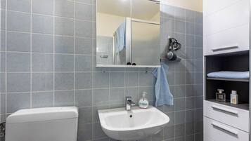 A bathroom with a white sink, a mirror, a towel hanging on the wall, and a shower area.