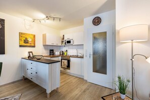 A modern kitchen with white cabinetry, a microwave, a coffee maker, and a clock on the wall.