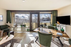 Een moderne woonkamer met een groot raam, een flatscreen televisie en een eethoek.