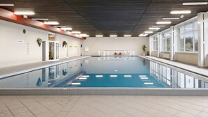 An indoor swimming pool with a tiled floor, clear pool water, and a ceiling with linear light fixtures.