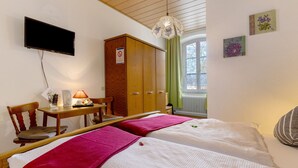 Une chambre d’hôtel avec deux lits, une télévision, une armoire en bois, un bureau avec une lampe et une fenêtre avec des rideaux.