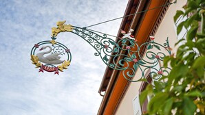 Une enseigne représentant un cygne, agrémentée d’une arche décorative, fixée à un bâtiment doté d’une fenêtre et d’une porte.
