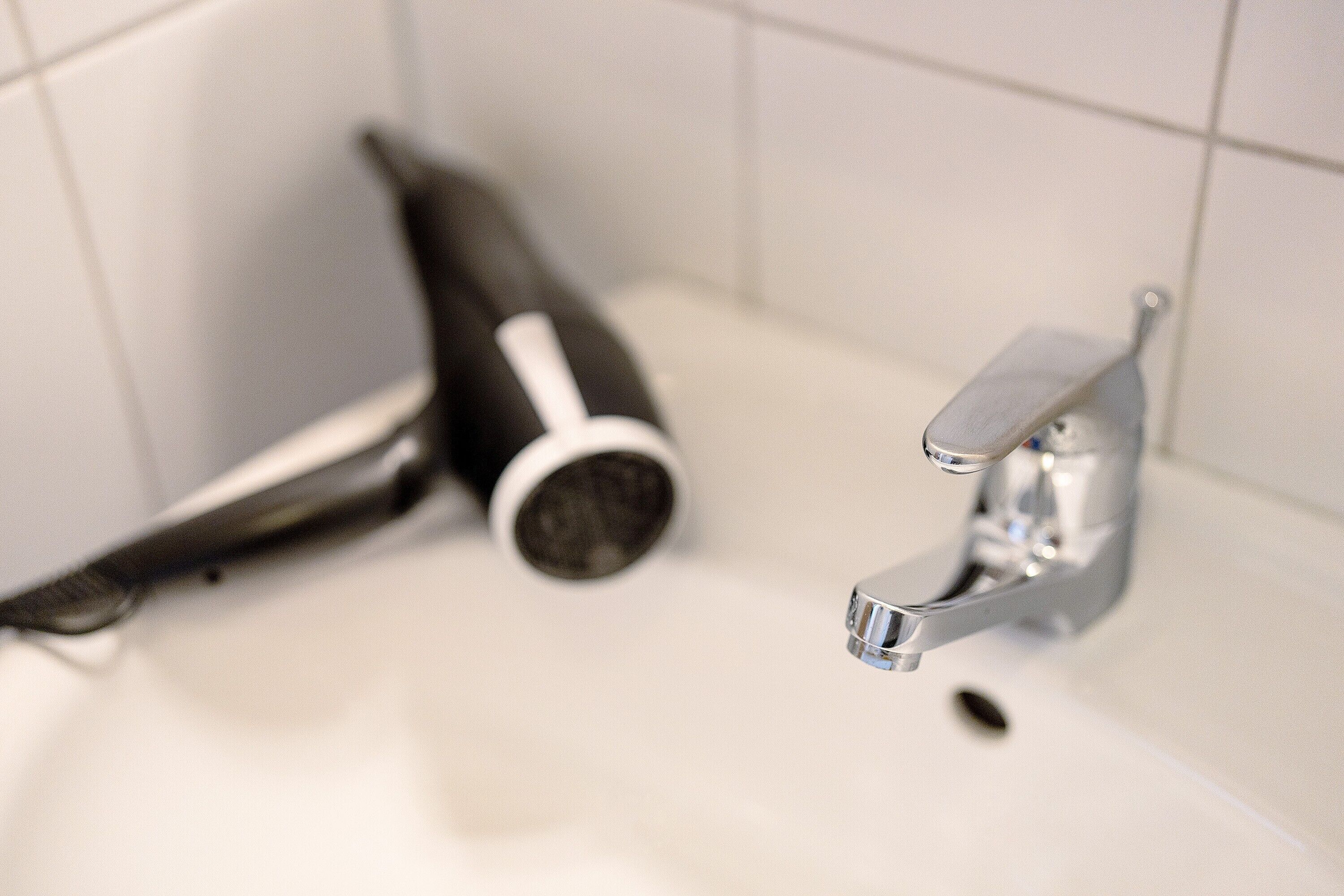 Ein Badezimmer mit einem weißen Waschbecken, einem Fön und einem Wasserhahn.