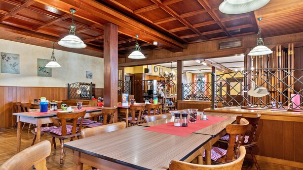L’intérieur d’un restaurant avec des tables et des chaises en bois, des luminaires suspendus et un coin bar.