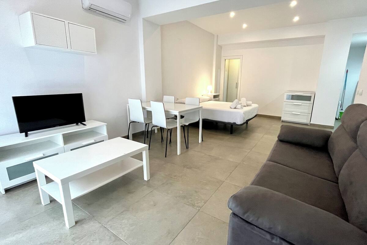 Un salon moderne doté d’un téléviseur à écran plat, d’un canapé, d’une table à manger avec des chaises et d’un lit avec une table de chevet.