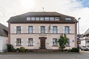 A two-story building with a sign reading 'Schwanen' at the entrance, a small porch with steps, and a street view with a speed limit sign. - Room 'Doppelzimmer 9' with Shared Terrace (Oberkirch)