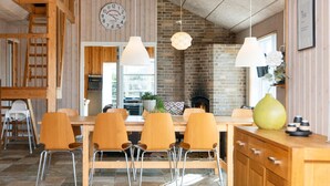 Un coin repas avec une cheminée en briques, des chaises en bois et une horloge au mur.