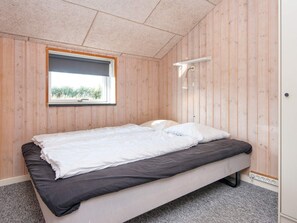 Un lit simple dans une pièce aux murs en bois et dotée d’une fenêtre.