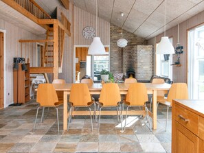 A spacious dining area with a long wooden table and six chairs, a brick fireplace, and a wooden staircase.