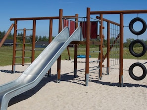 Un parque infantil con tobogán, estructuras de escalada y columpios de neumático.