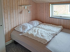 A single bed with a white duvet and pillows, a wooden wall, a window with a view of the outside, and a wall-mounted light fixture. - 4 Star Holiday Home in Tarm (Tarm)