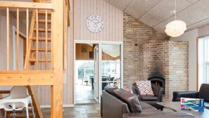 Un intérieur chaleureux avec une cheminée en briques, des fauteuils en cuir et un escalier en bois.