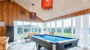 Une table de billard dans une pièce dotée de grandes fenêtres, un jeu de billard et un coin salon confortable.
