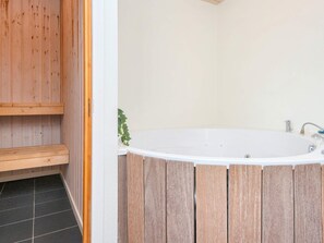 Un baño con una bañera de madera, un lavamanos blanco y una planta verde.