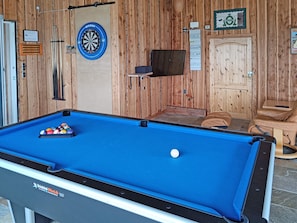 Una mesa de billar con bolas, un dardo y una televisión fijada en una pared de madera.