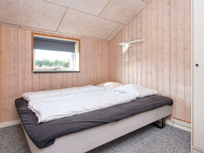 A single bed with a white and dark mattress, a window with a view of greenery, and a wall-mounted light fixture. - 4 Star Holiday Home in Tarm (Tarm)