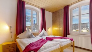 Une chambre avec deux lits, une table de chevet, une fenêtre avec des rideaux et un radiateur.