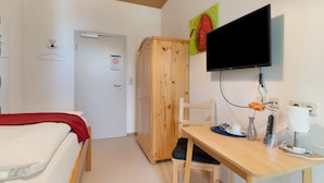Een hotelkamer met een bed, een bureau met een computer, een televisie, een kledingkast en een deur.