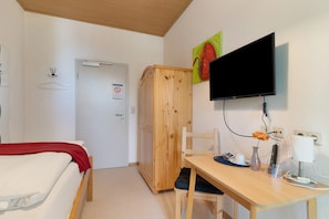 Une chambre d’hôtel avec un lit, un bureau avec un ordinateur, une télévision, une armoire et une porte.