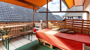 Een overdekt buitengebied met een houten bed, banken en een tafel.