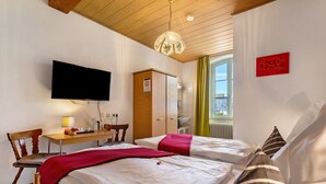 Habitación de hotel con dos camas, un escritorio, una silla, un televisor y una ventana con cortinas.
