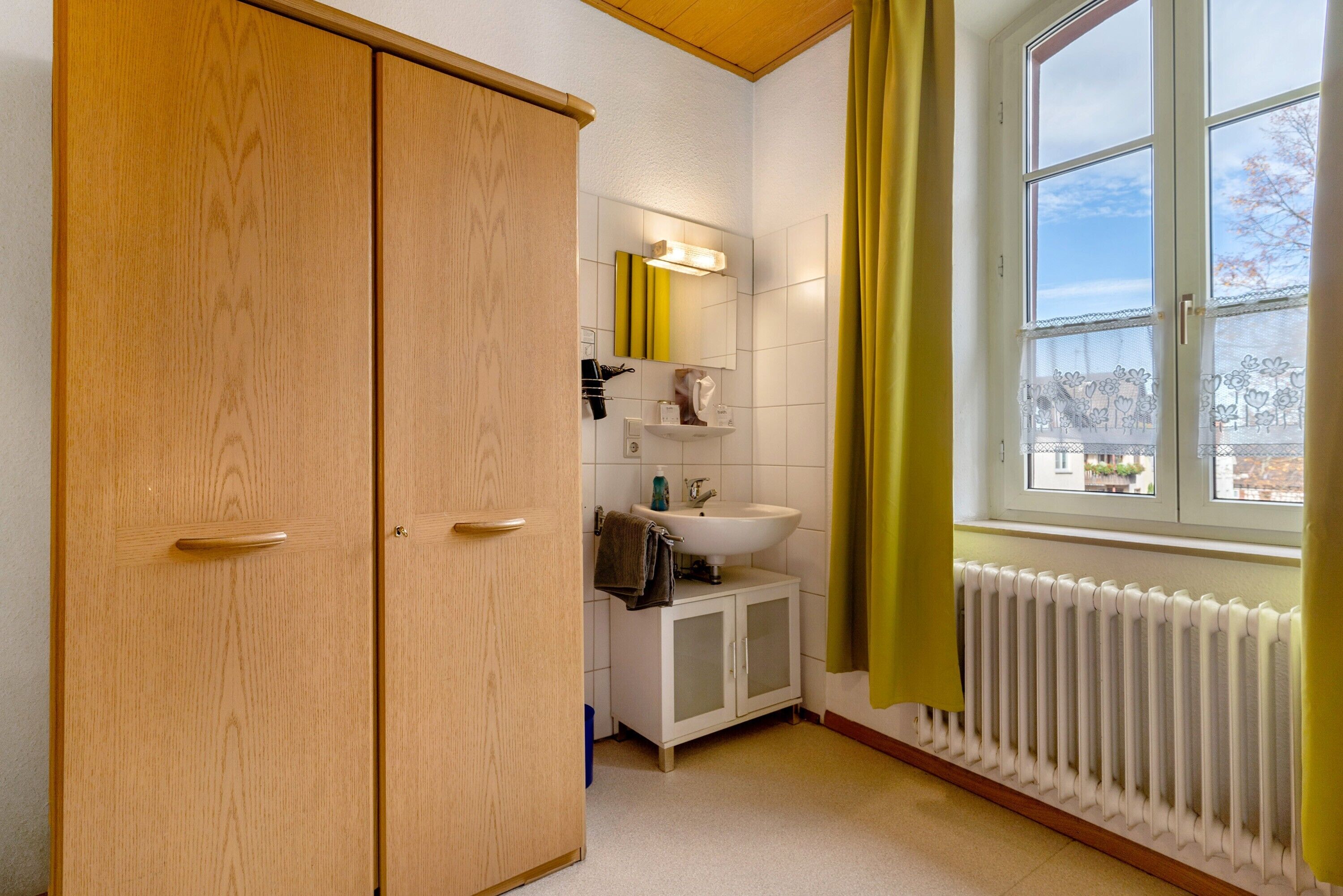 Ein Badezimmer mit einem Holfischschrank, einem Waschbecken, einem Spiegel und einem Fenster mit Vorhängen.