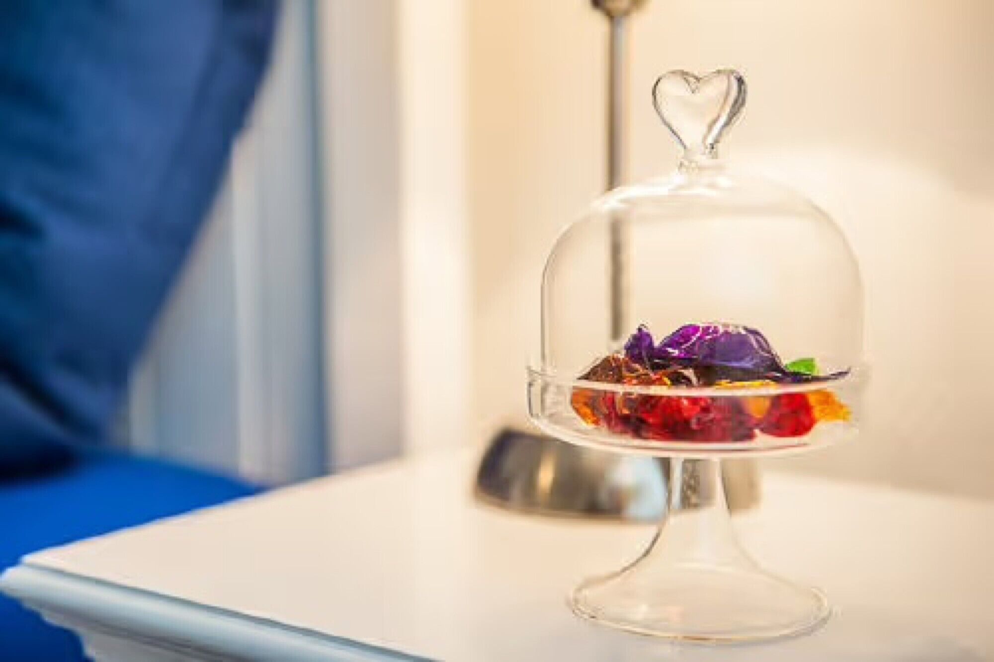 A dessert under a glass dome with a heart-shaped topper on a white table.