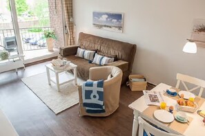 A living room with a sofa, a coffee table, a dining table with breakfast items, and a view through a glass door.