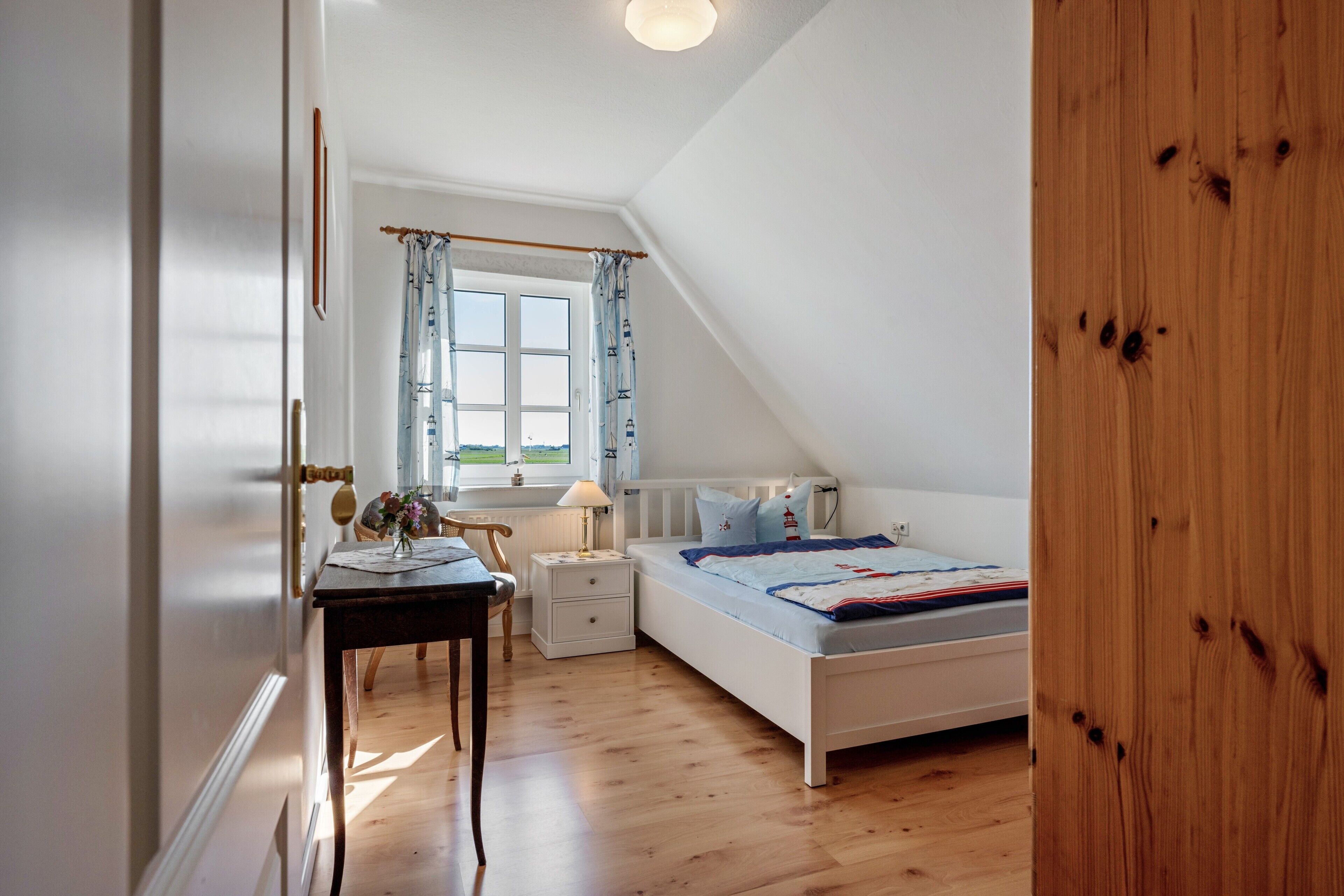 Een slaapkamer met een bed, nachtkastje, bureau, stoel, raam met gordijnen en uitzicht op de omgeving.