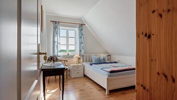 Een slaapkamer met een bed, nachtkastje, bureau, stoel, raam met gordijnen en uitzicht op de omgeving.