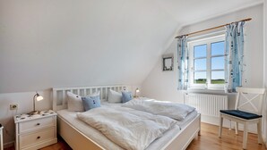 Et soveværelse med seng, natbord, stol og et vindue med gardiner.