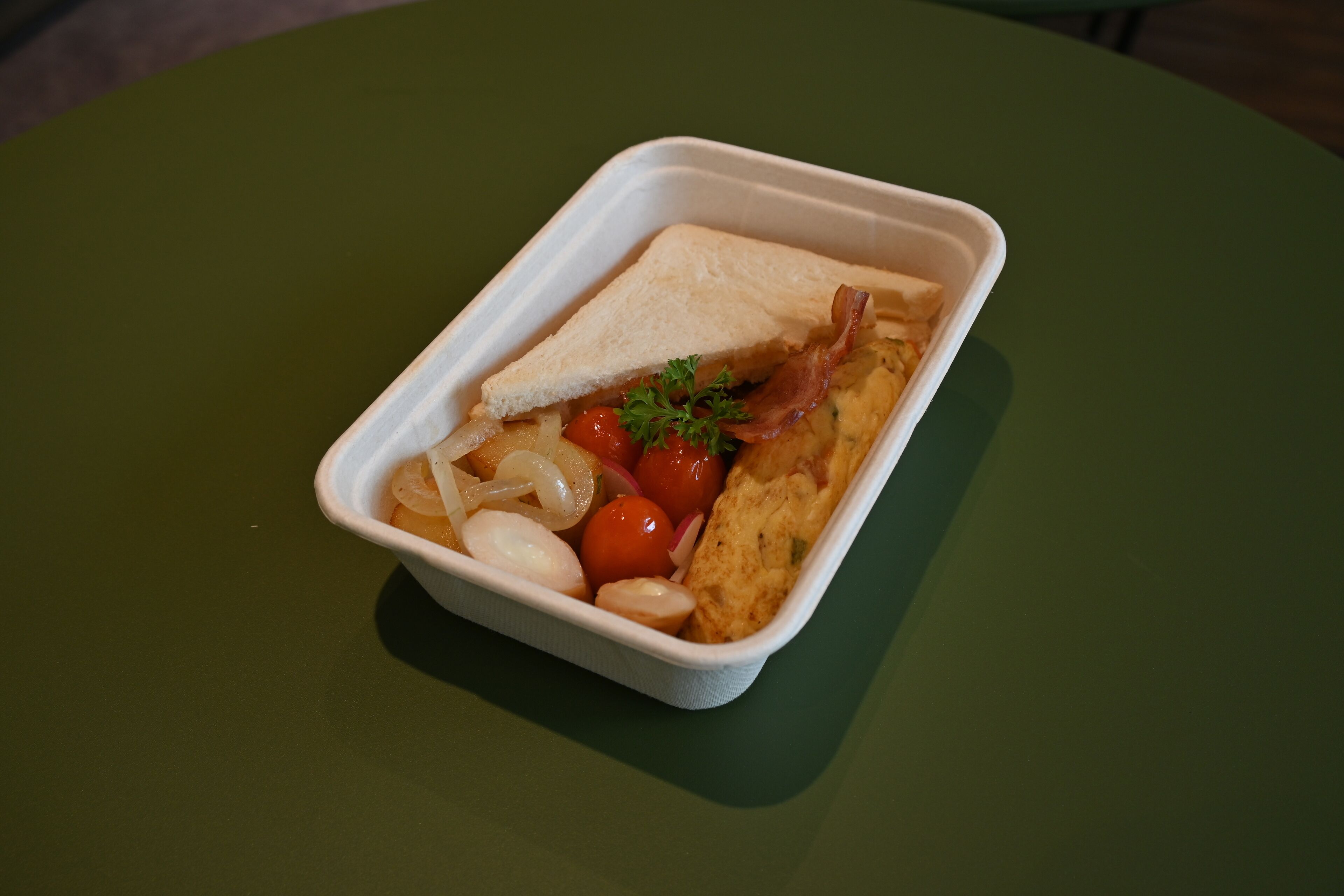 Eine Mahlzeit in einem weißen Transportbehälter auf einem grünen Tisch.