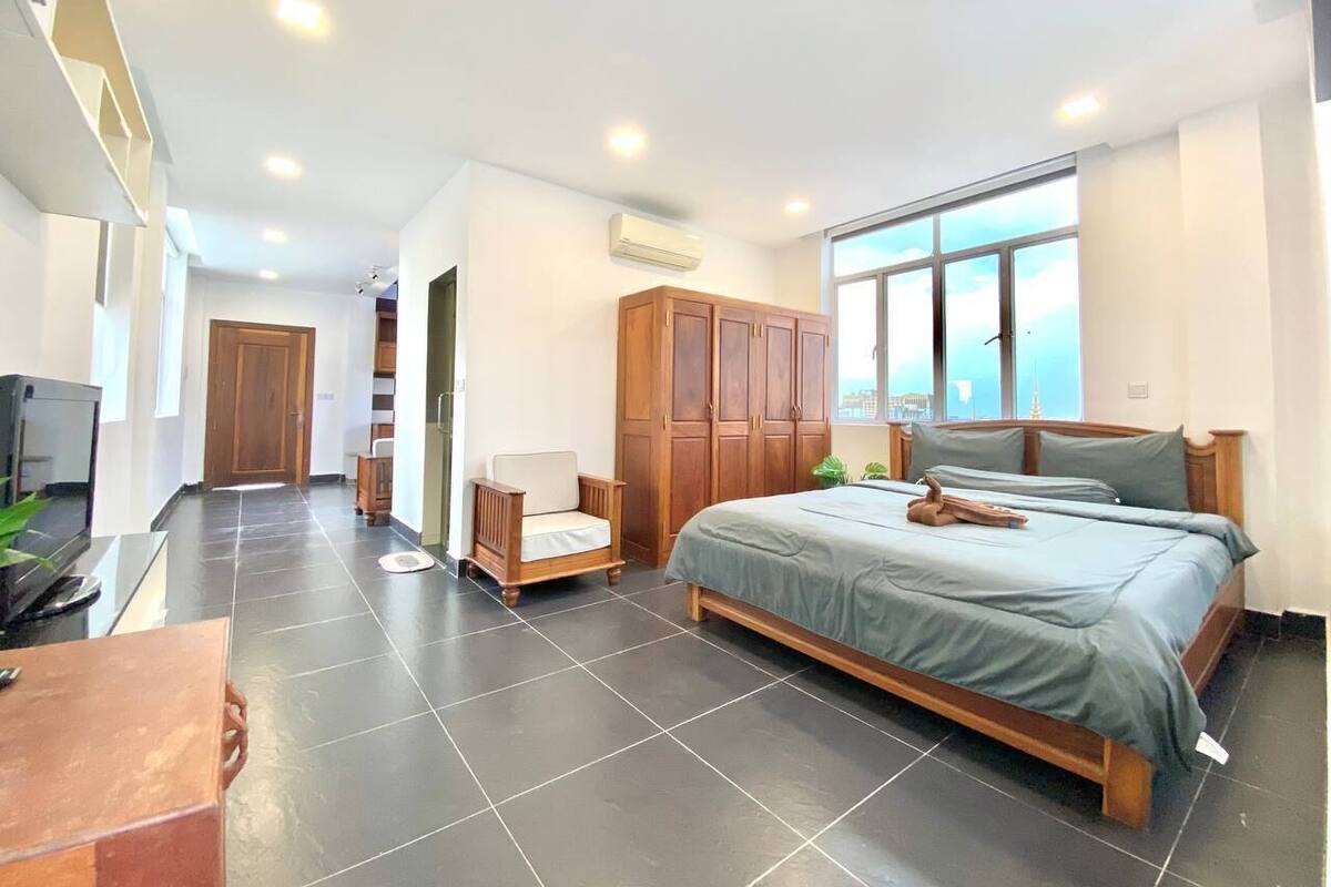 A modern bedroom with a large bed, a wooden wardrobe, a chair, and a desk with a plant.