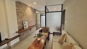 A modern living room with a brick accent wall, a wooden coffee table, a beige sofa, and a glass partition. - WH Bassac Residence  (Phnom Penh)