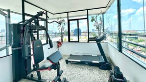 A modern gym with a treadmill, weight machine, and a bench. It has large windows offering a city view. - WH Bassac Residence  (Phnom Penh)
