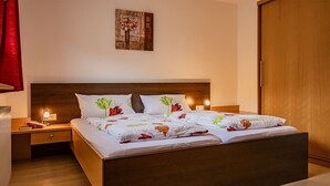 A neatly made bed with floral bedding, a wooden headboard, bedside lamps, and a nightstand with a lamp and books.