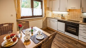 A dining area with a table set for two, a kitchen with white cabinets and a stove, and a window with curtains.