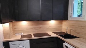 Une cuisine de taille réduite, avec des meubles de couleur sombre, un lave-linge et un lave-vaisselle.