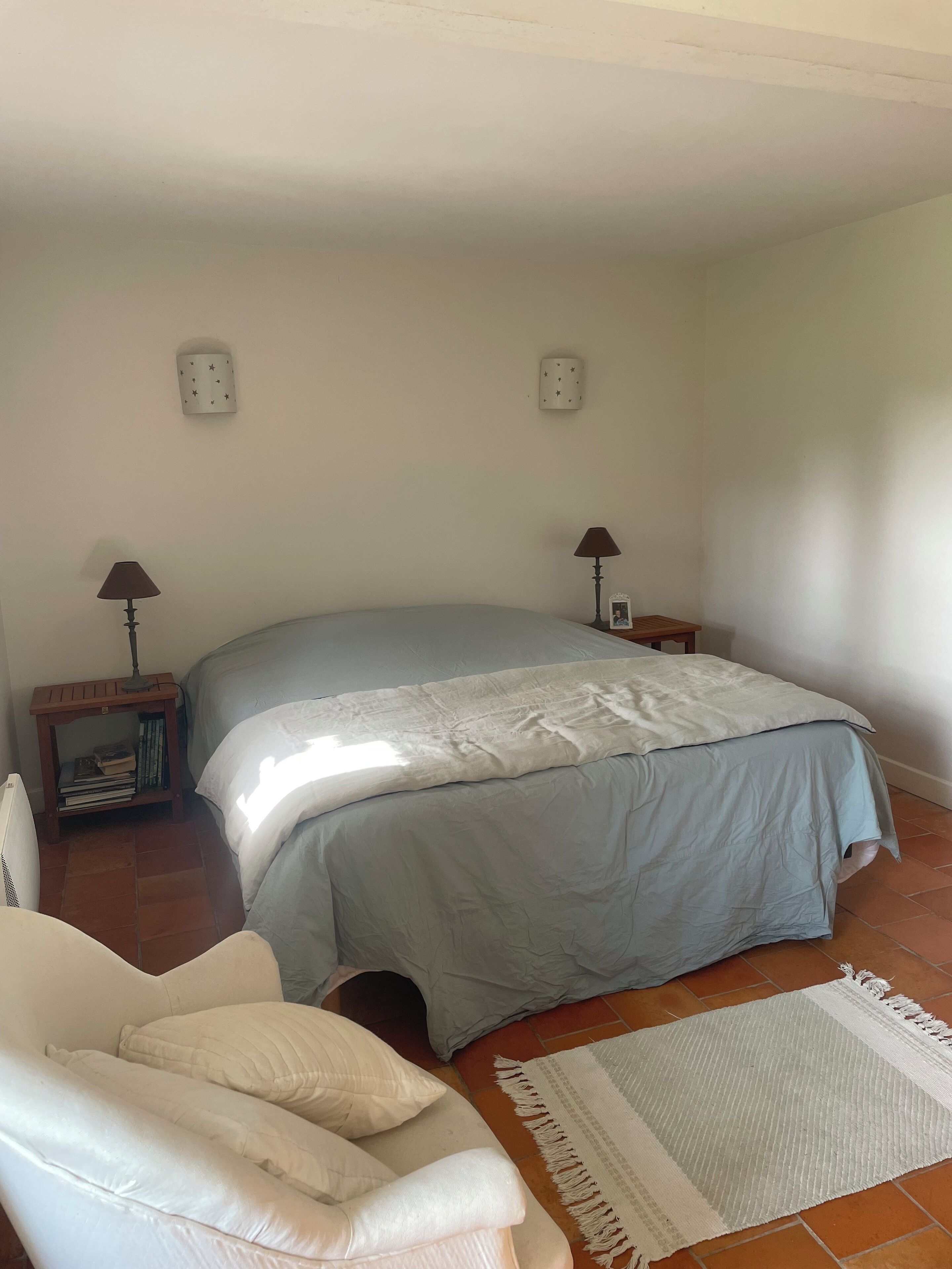 A bedroom with a bed, bedside lamps, a chair, a rug, and a small table with books.