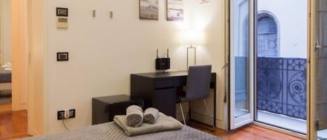 A bedroom with a bed, a desk, a chair, and a balcony with a view.
