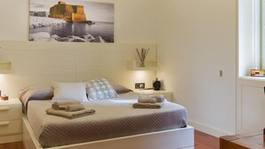 Un dormitorio con cama, mesitas de noche, un cuadro y una ventana.