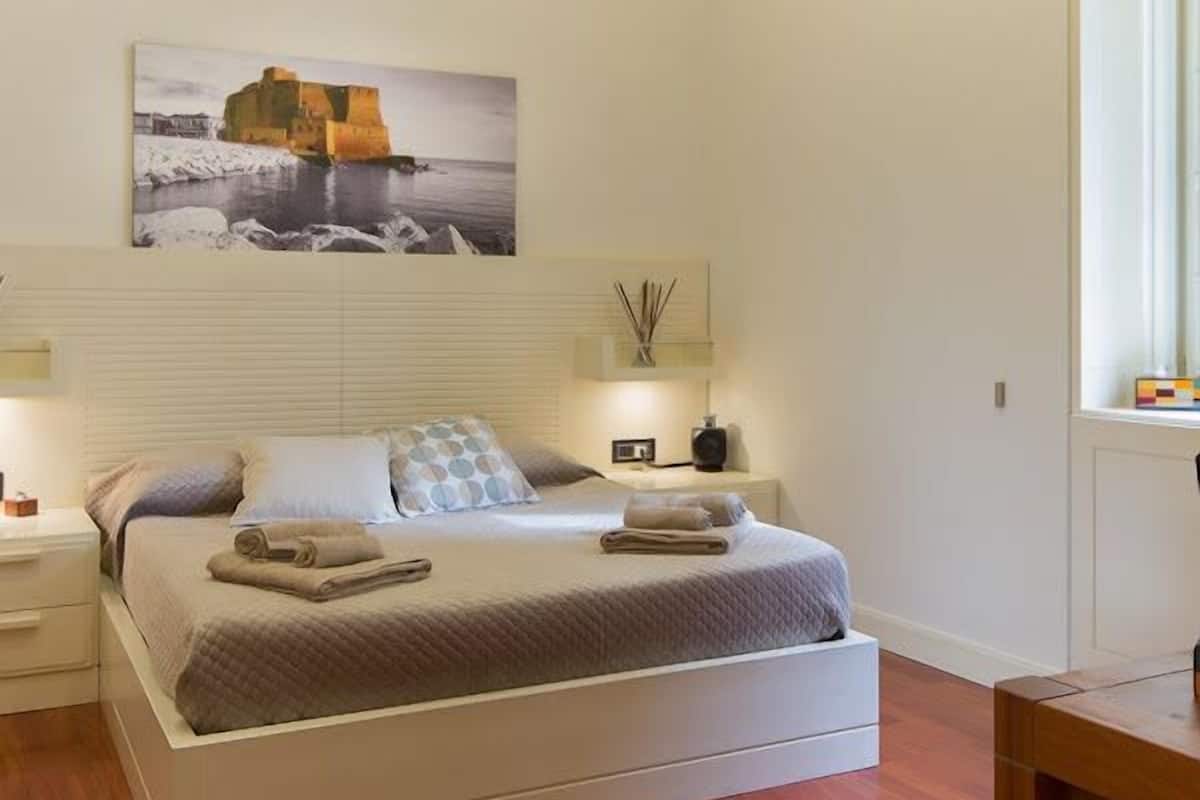 Une chambre à coucher avec un lit, des tables de chevet, une commode, un tableau et une fenêtre.