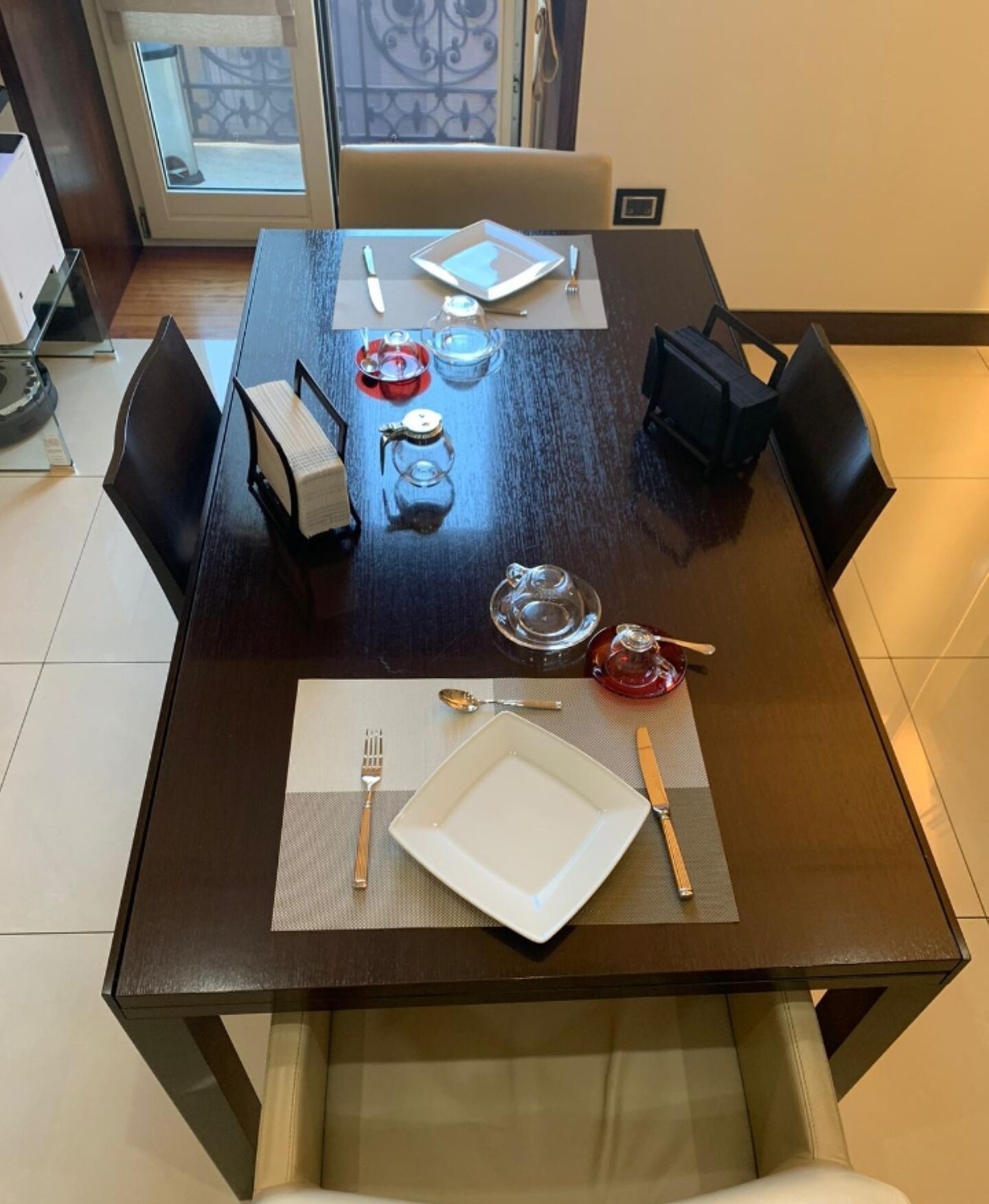 Una mesa de comedor dispuesta con platos, cubiertos y vasos, rodeada de sillas.
