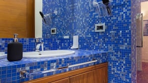 Un baño con pared de mosaicos azules, tocador de madera con lavabo y espejo.