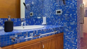 Un bagno con parete rivestita in mosaico blu, un mobile bagno in legno con lavandino e uno specchio.