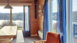 Una cabaña de madera con una mesa y sillas de comedor, un sofá y un ventanal con cortinas.