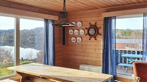 Interior de madera con una gran mesa y bancos, un reloj de pared y vistas al exterior.