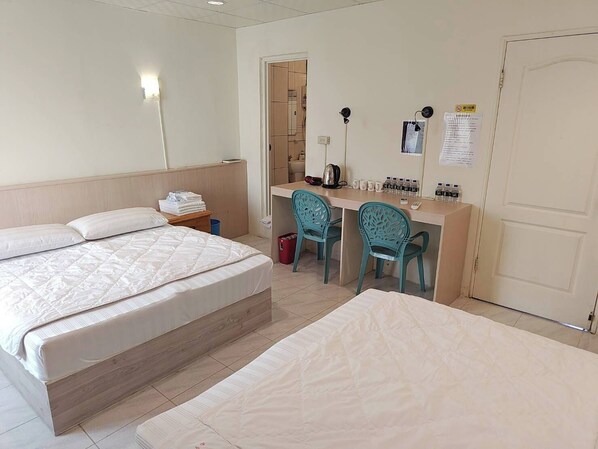 Une chambre d’hôtel avec deux lits, un bureau avec des chaises, une lampe et une porte.